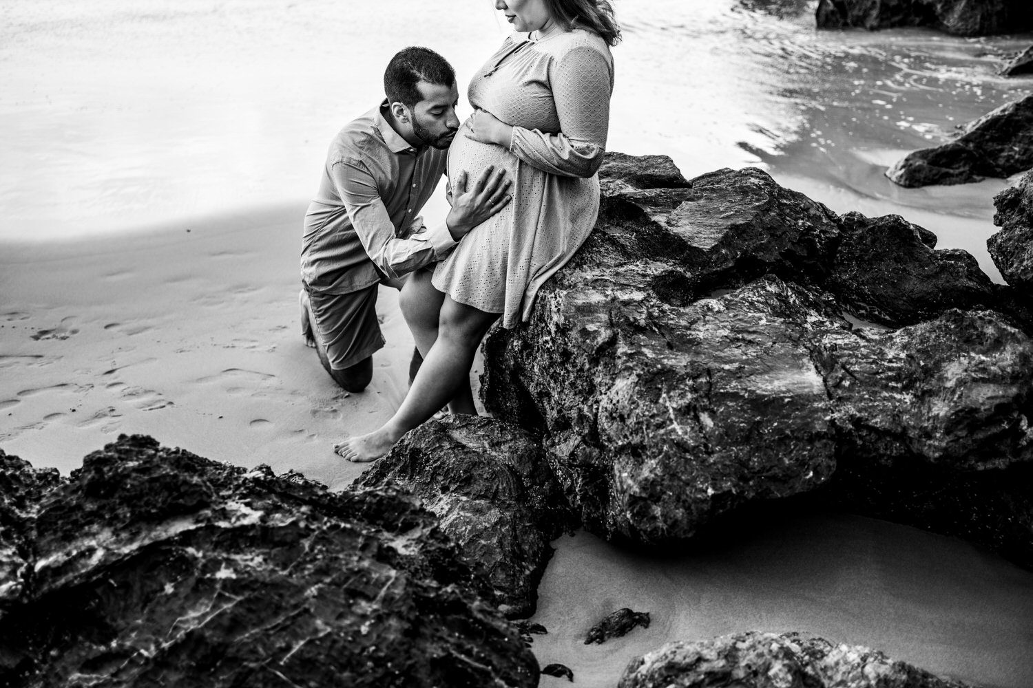 padre besando la barriga embarazada de su esposa en la playa