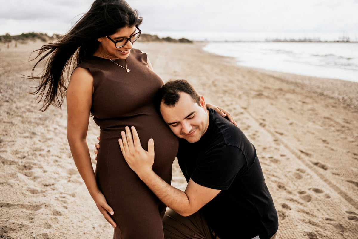 padre escuchando la barriga de su esposa embarazada en la playa