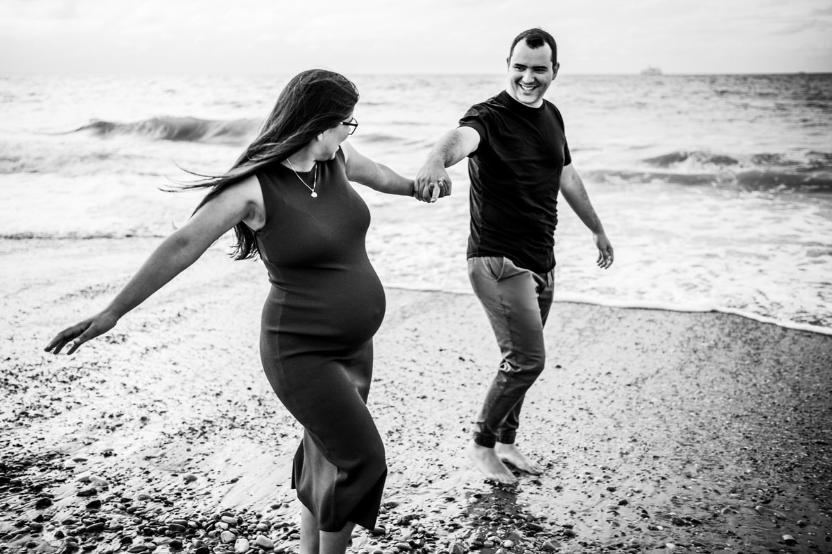 pareja feliz caminando en la playa embarazada
