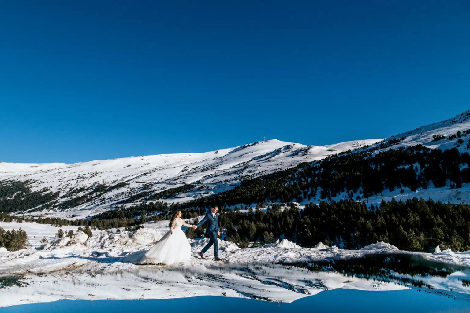 couple walking through the snow surrounded by mountains and a reflection, destination wedding photographer in Andorra