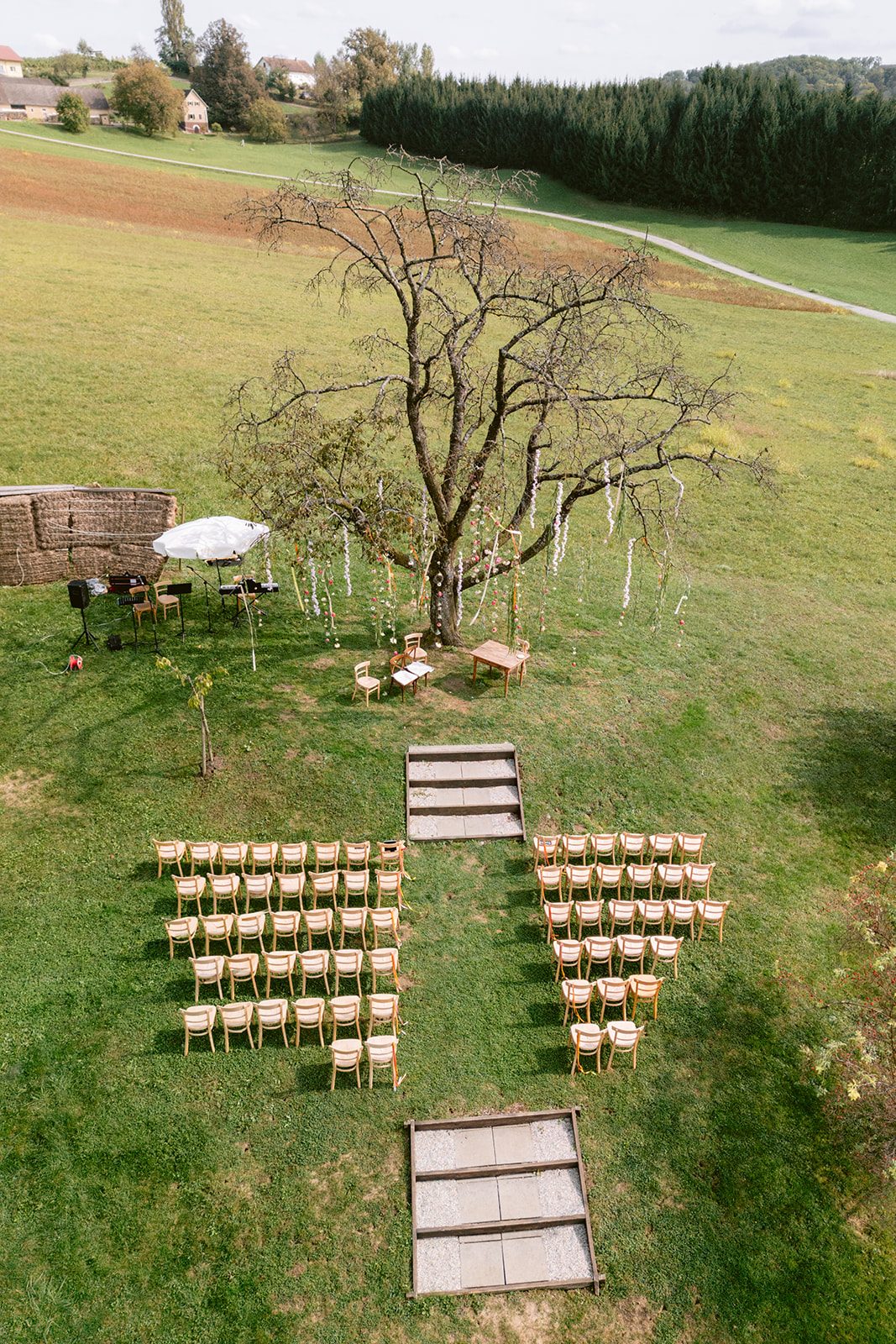 Drone shot showing outdoor vineyard wedding ceremony setup with rows of chairs and central tree at Weingut Holler, Austria