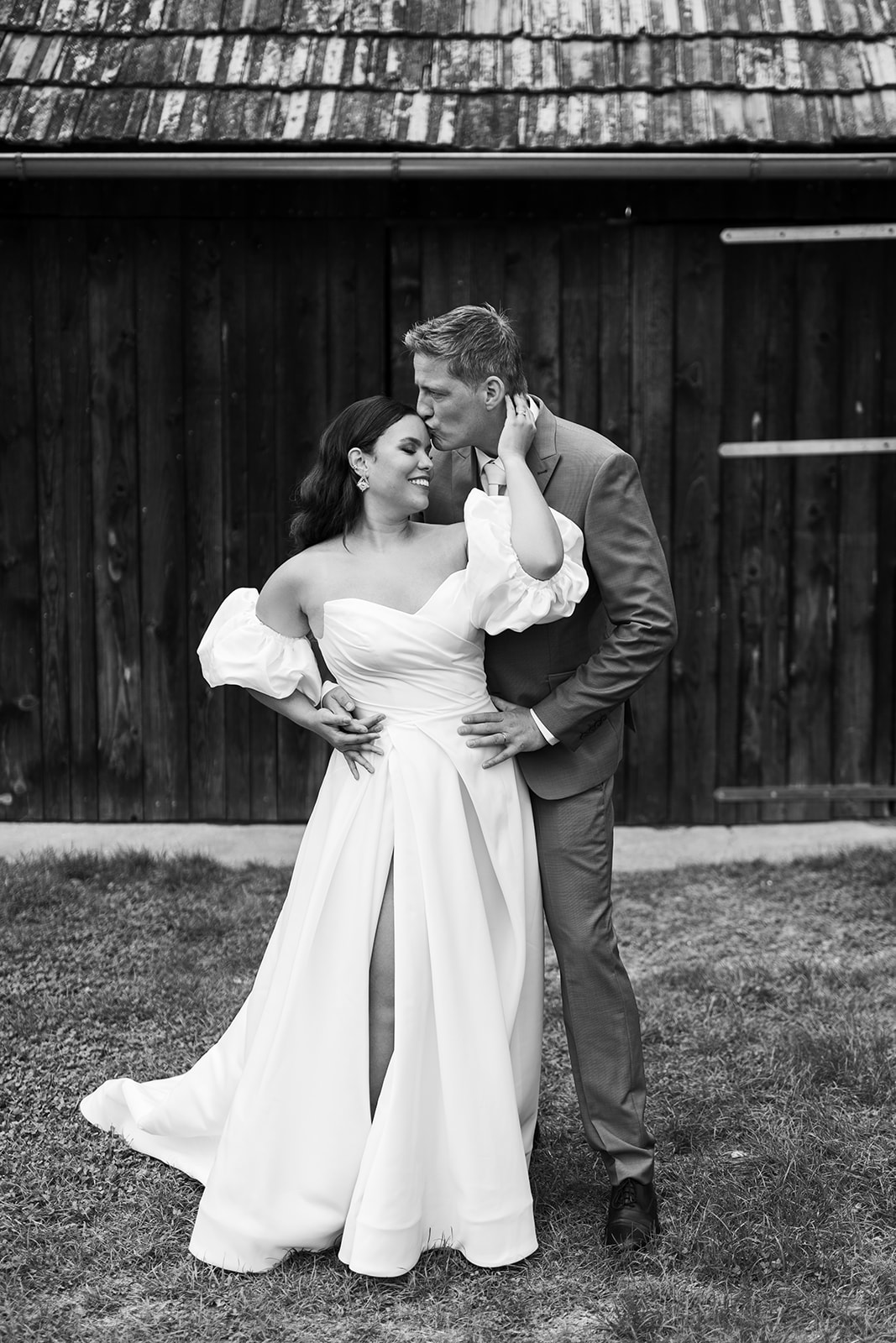 Bride and groom posing in front of rustic barn and scenic farm landscape at Weingut Holler vineyard wedding