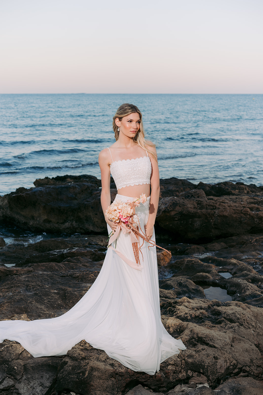 Elegant blonde bride in a stylish gown posing by the sea during a romantic Mediterranean styled shoot.