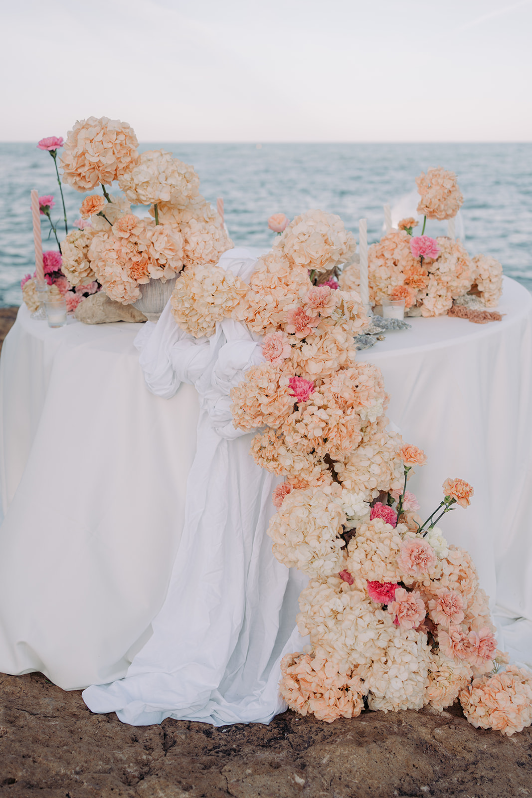 Elegant wedding table setup by the Mediterranean Sea, featuring floral arrangements, candles, and rustic charm.