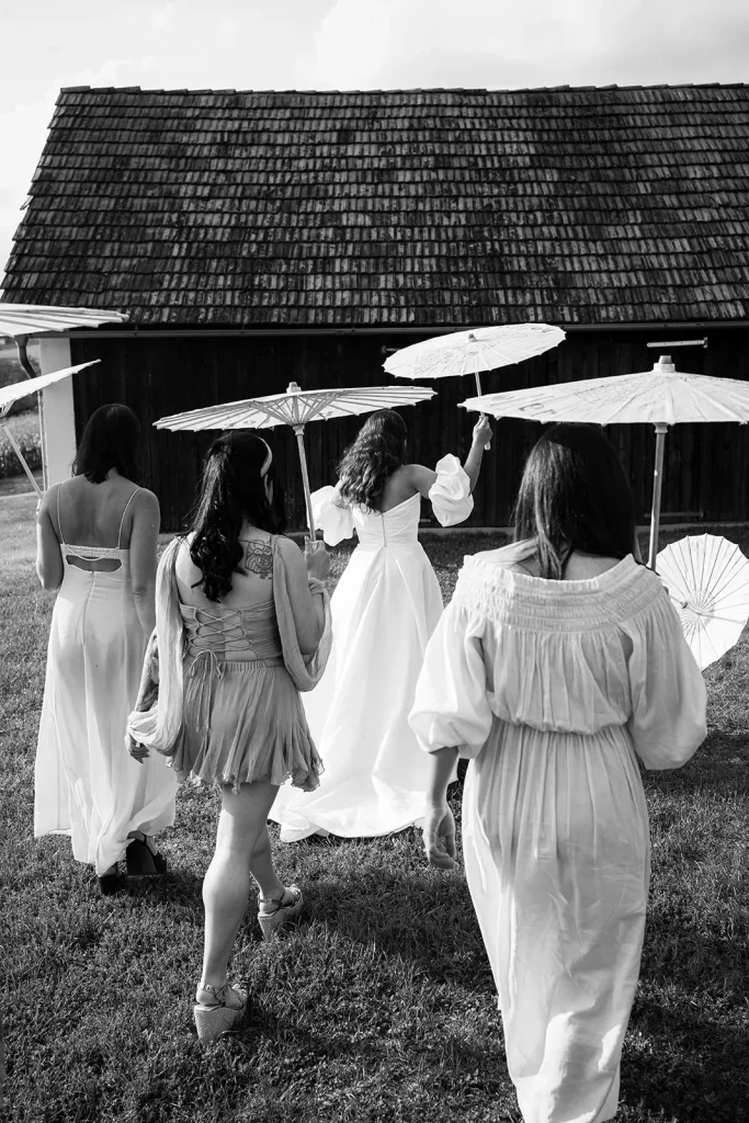 Bridesmaids posing with clear umbrellas during a light rain shower at a vineyard wedding, adding an editorial and romantic touch
