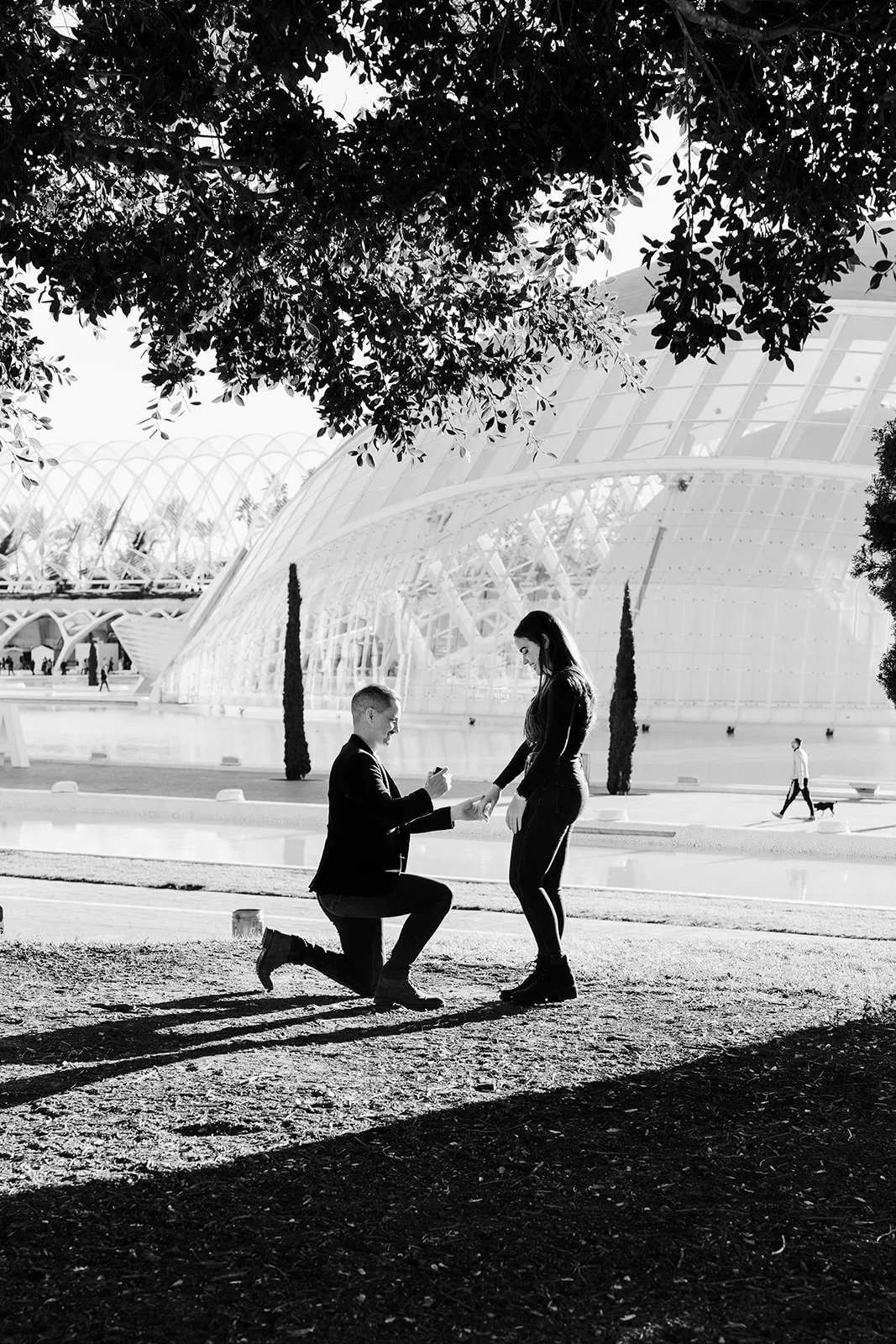 Groom-to-be kneeling and proposing to his partner in front of the modern architecture of Ciudad de las Artes y las Ciencias.